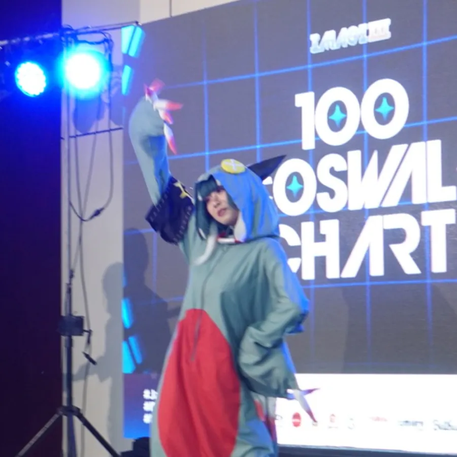 Seorang cosplayer tampil di atas panggung 100 Coswalk Chart dengan layar LED bertuliskan nama kompetisi di belakangnya.